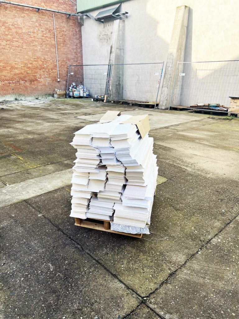Pile de chutes de papier blanc réutilisable empilées sur une palette en extérieur, destinée à la fabrication de carnets écologiques par Odd Paper